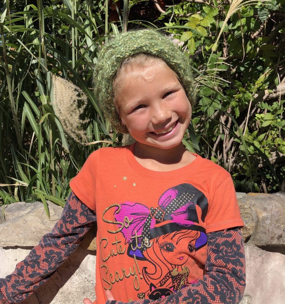 a young girl smiles while wearing a knitted cabled headband