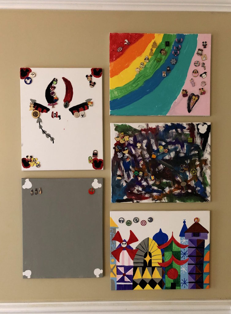 five painted canvases that display Disney collector pins hang on a wall