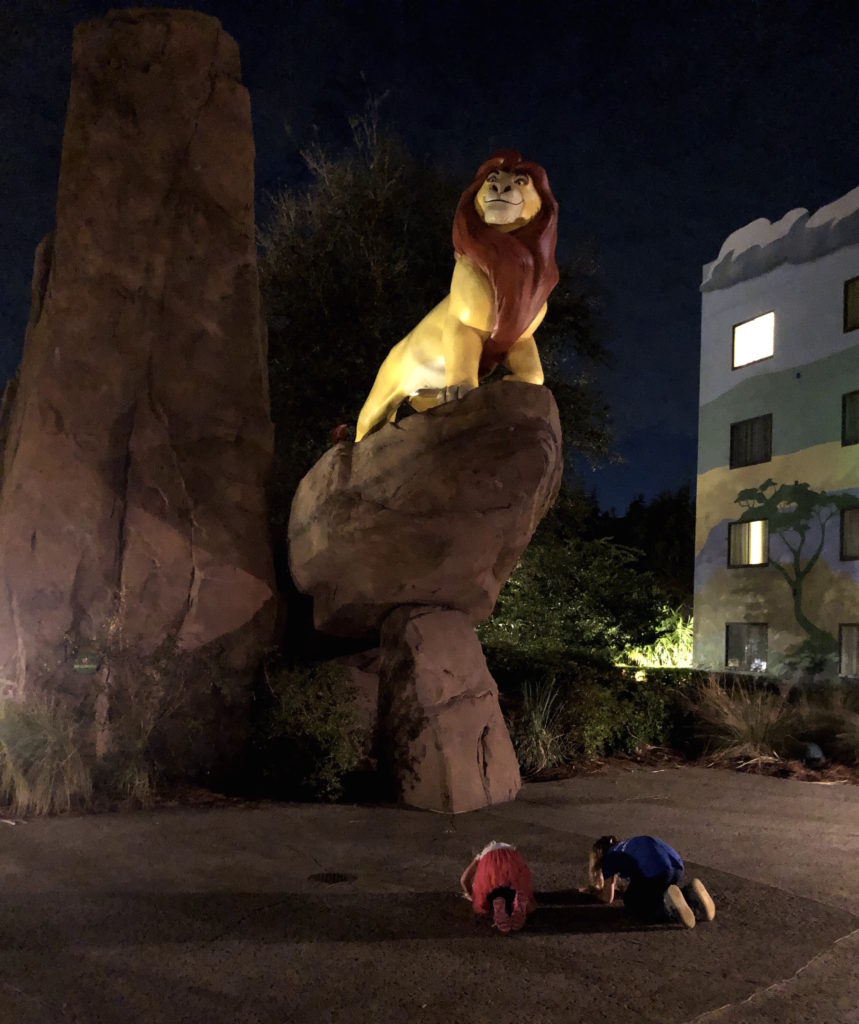 two children kneel before a statue of Simba on Pride Rock 