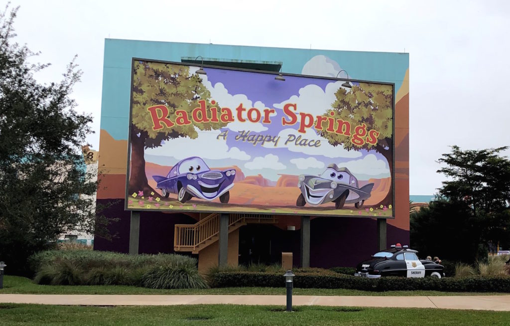 a sign featuring two smiling cars welcomes visitors to Radiator Springs: A Happy Place