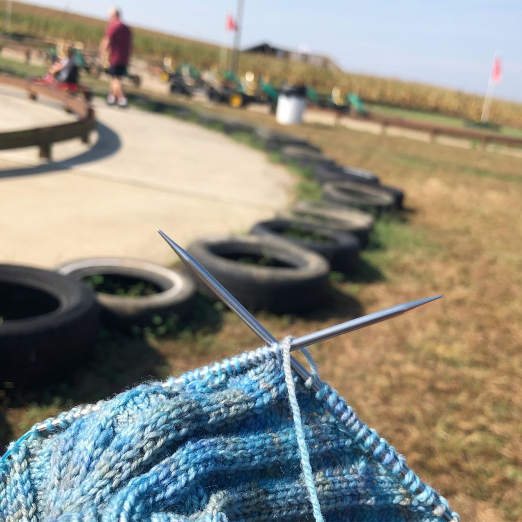 knitting needles work on a project in the foreground while children play on pedal cars in the background