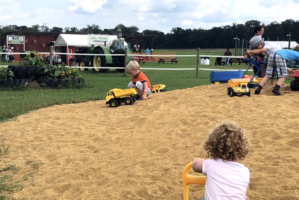 a child plays with a dumptruck in a large pile of dried corn