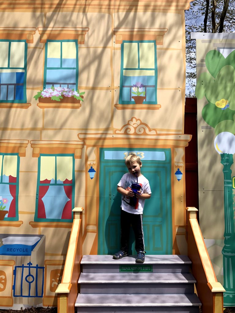 a boy poses on the top stoop of a house on Sesame Street