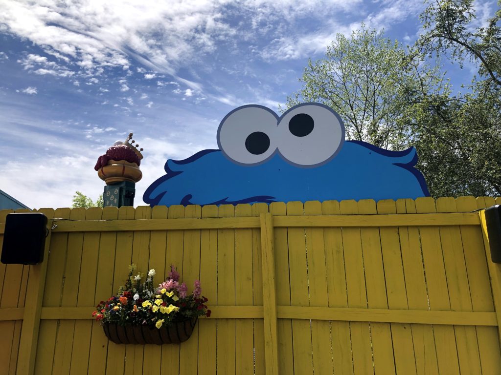 a jumbo Cookie Monster cut-out peeks over a colorful fence