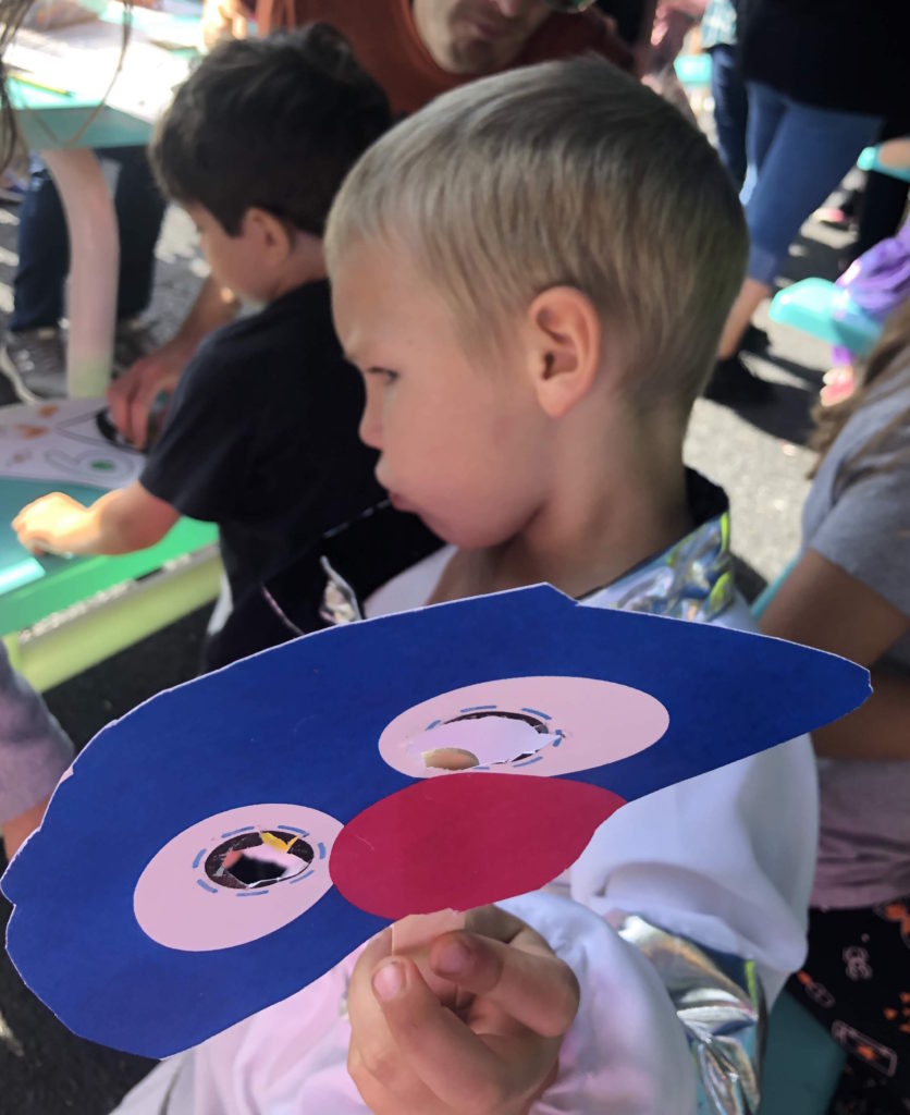 a child holds out a handmade Elmo mask craft