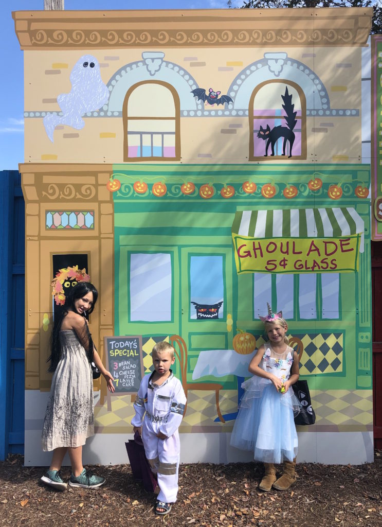 three children in Halloween costumes pose outside a Sesame Street building