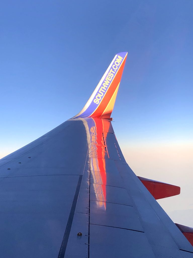 the wing of a Southwest airplane, taken from the window while the plane is in the air, bears the text "Southwest.com"
