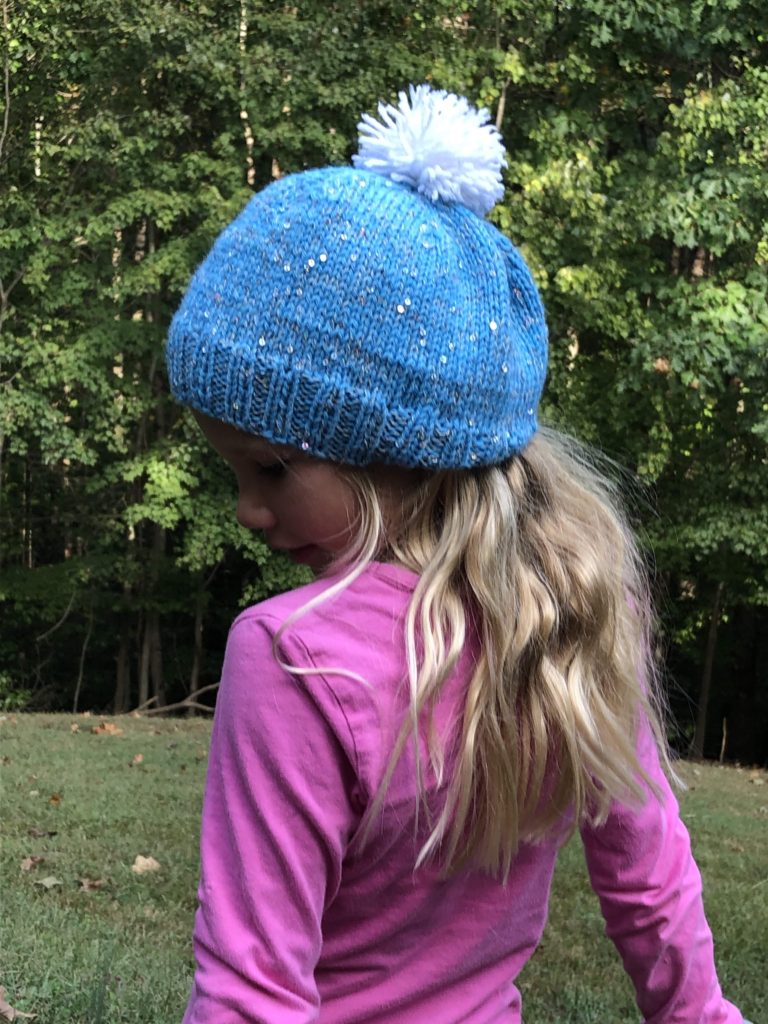 a child wearing a sparkling winter cap with pompom on top