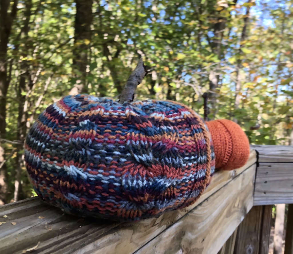 two knitted pumpkins, one in the background, on a ledge