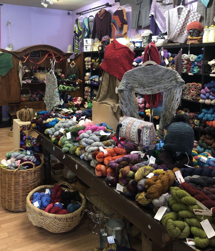 baskets and piles of yarn with a display of hand-knitted items
