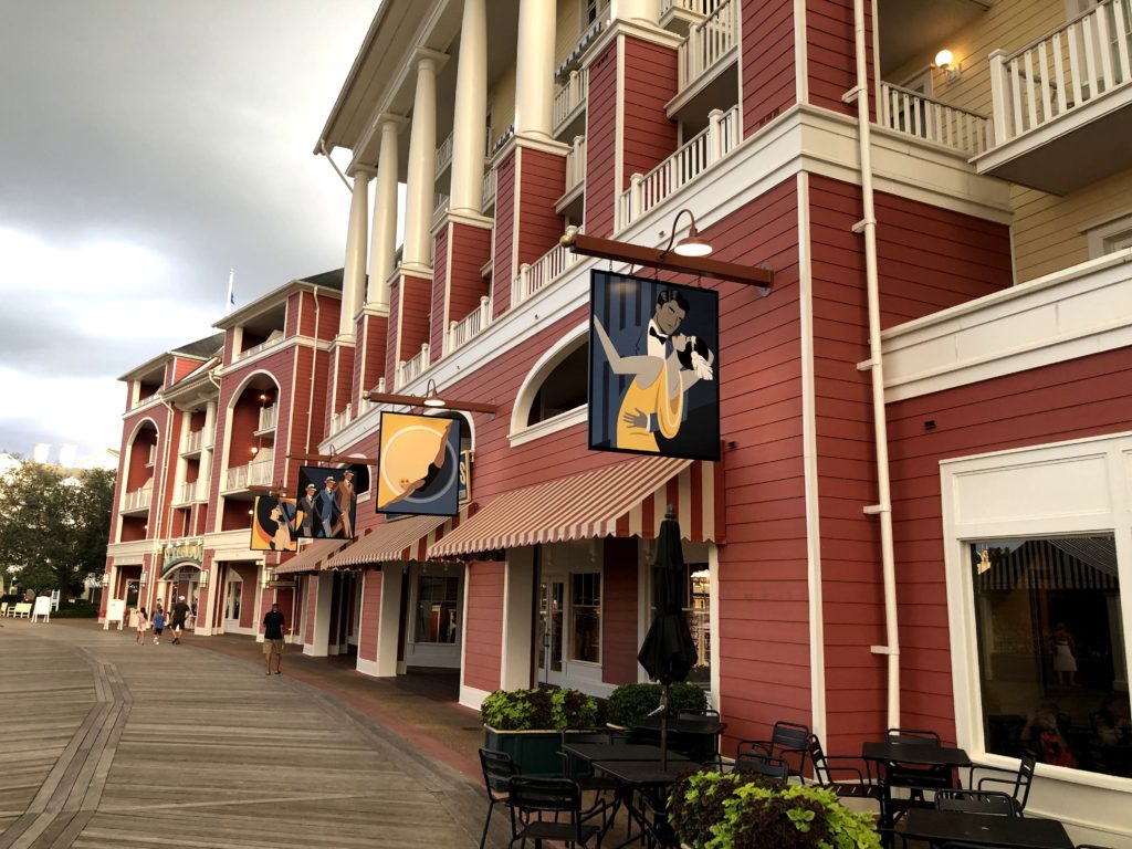 several shops with hanging signs face a wooden boardwalk