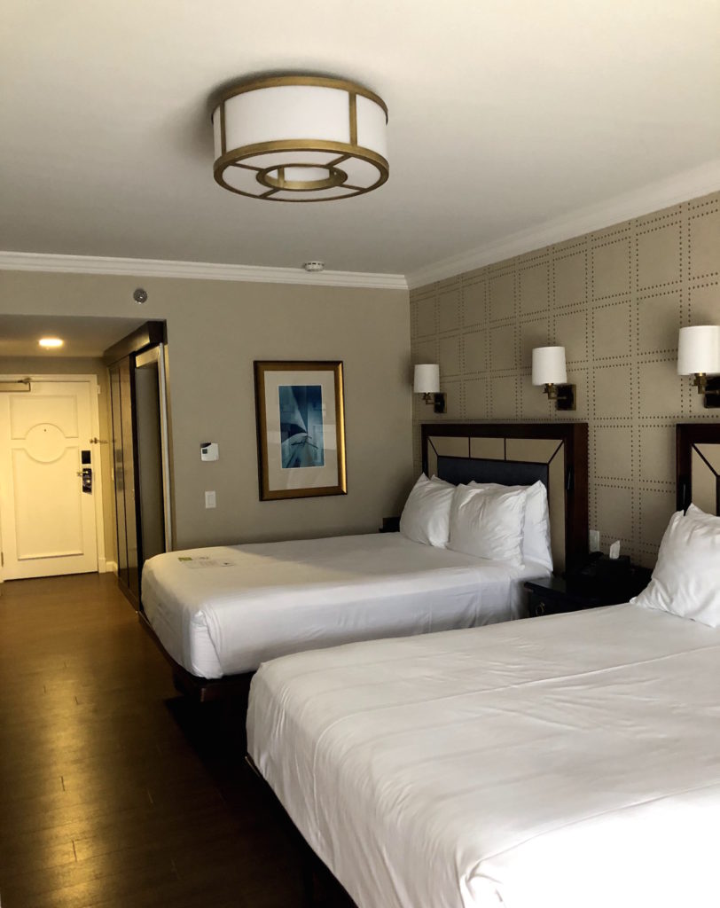 a hotel room with two beds, each with two lights above, and nautical wall art