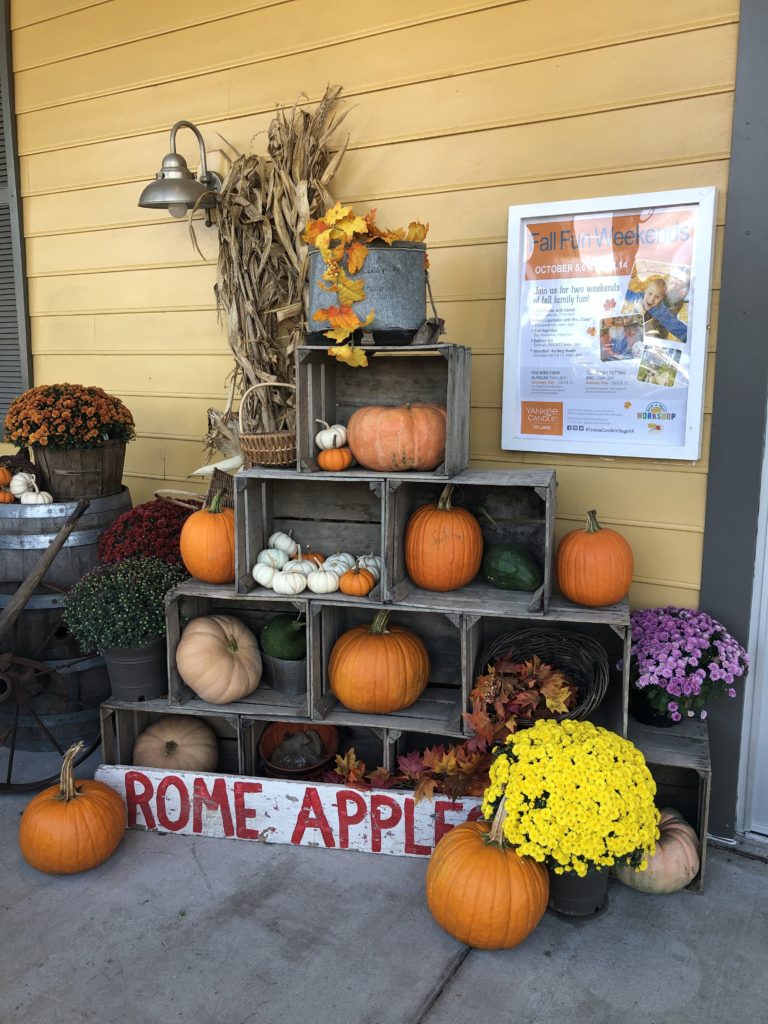 a fall display including sideways crates full of pumpkins, leaves, mums, and dried corn