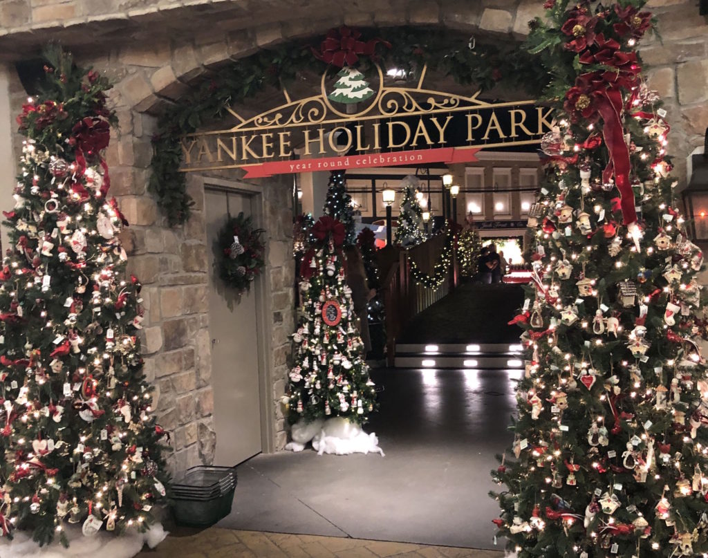 decorated Christmas trees surrounding a stone entryway with the words Yankee Holiday Park