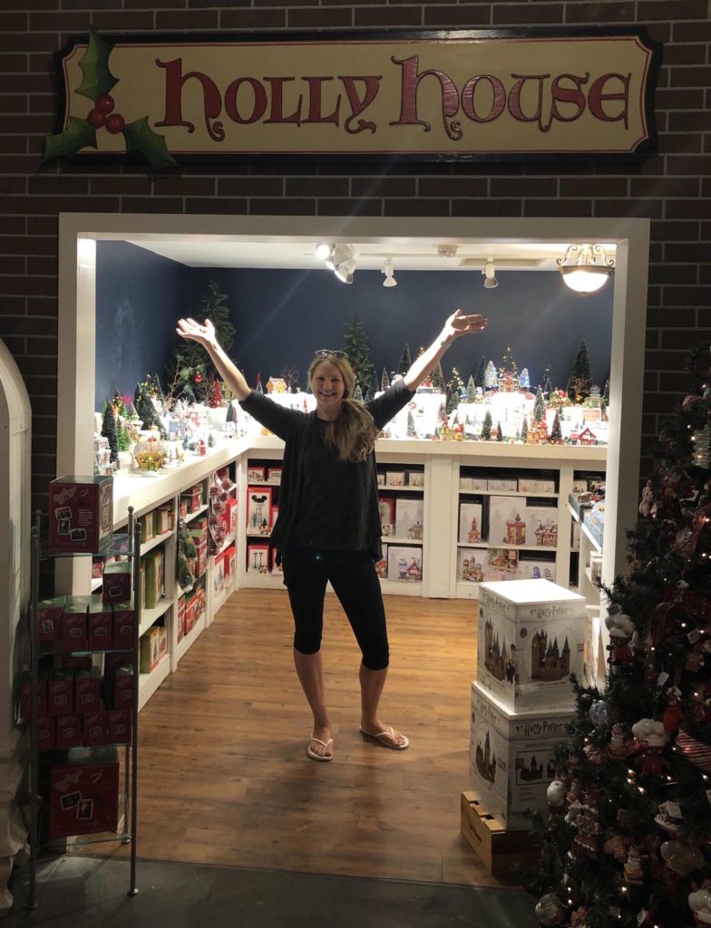 a woman standing with her arms up under a sign that reads Holly House