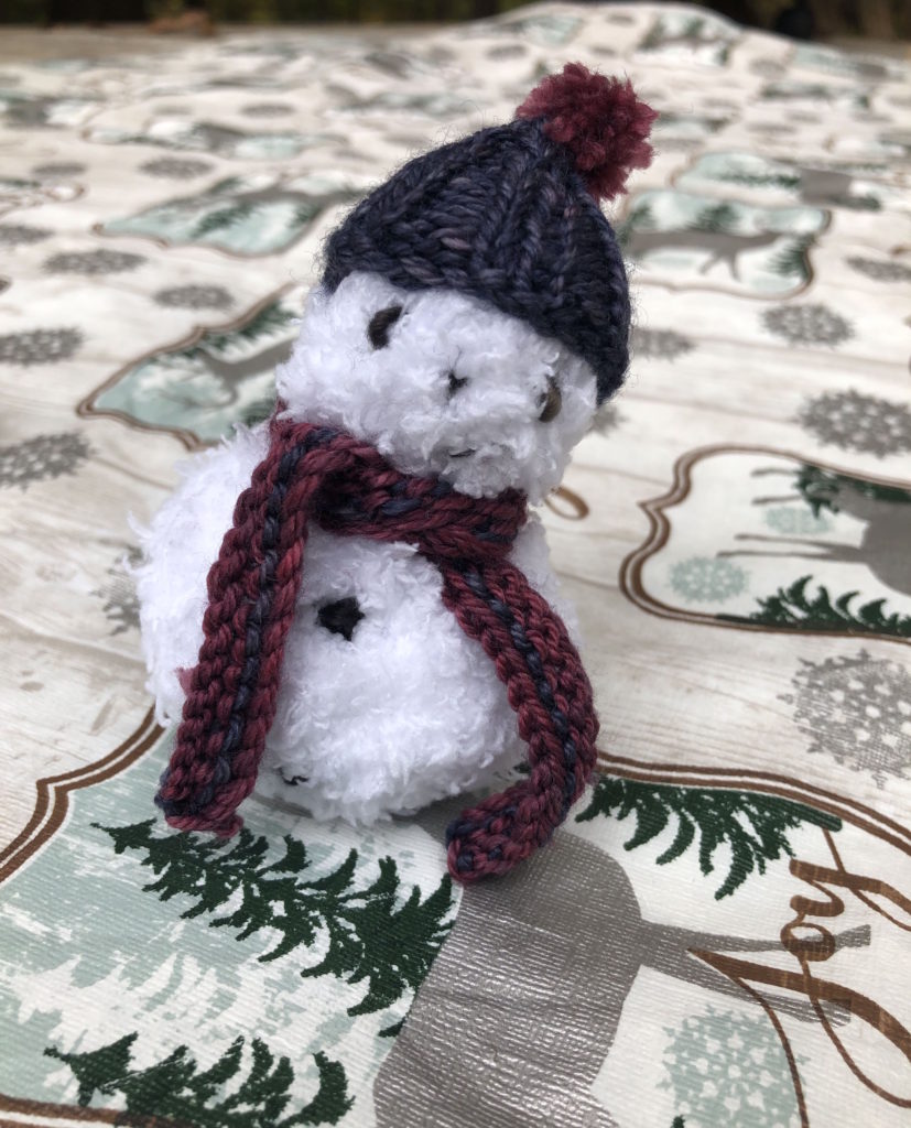 a knitted snowman wearing a blue hat and red and blue scarf (snowman knitting pattern)