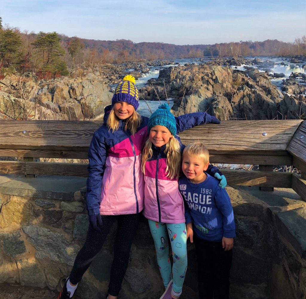 three children pose in front of a waterfall in knitted hats