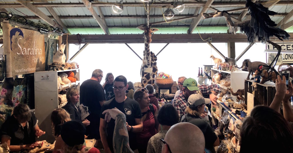 a crowd is packed into a fiber animal kit booth inside a barn at Maryland Sheep and Wool Festival