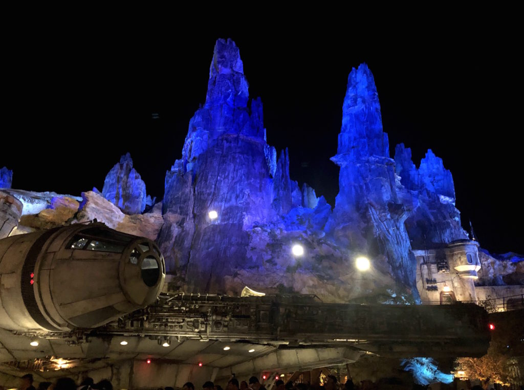 the Millennium Falcon in front of the craggy mountains of Batuu in the darkness of early morning