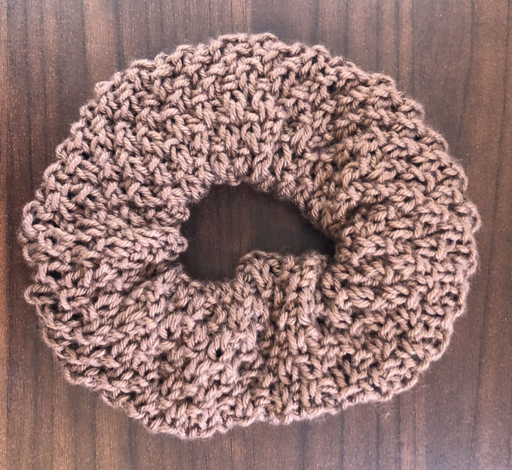 a textured knitted scrunchie on a wood panel background