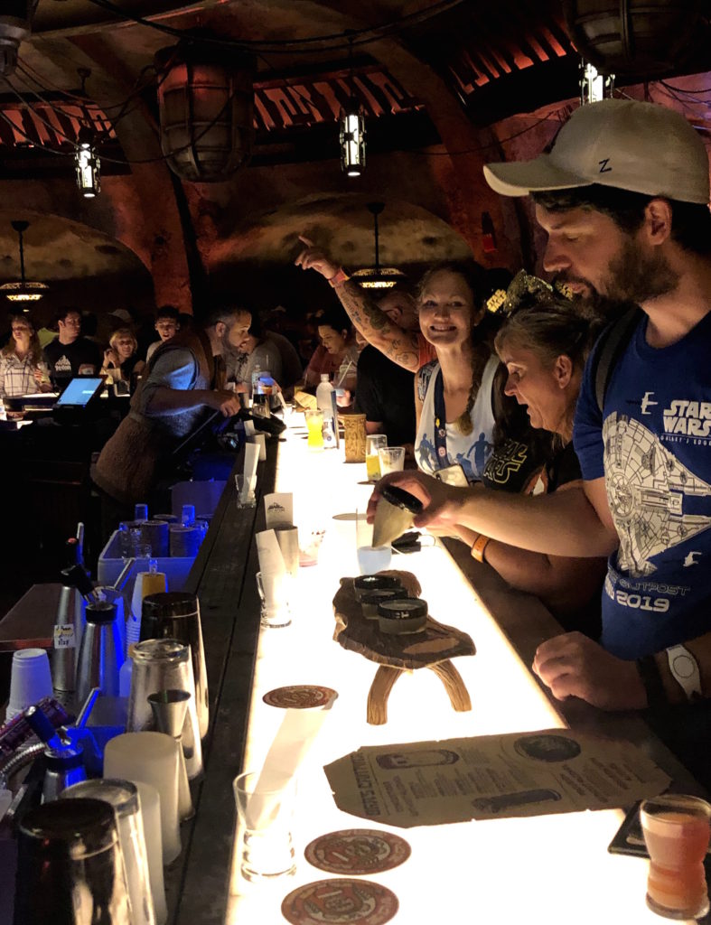 a woman at the bar of Oga's Cantina smiles at the camera excitedly