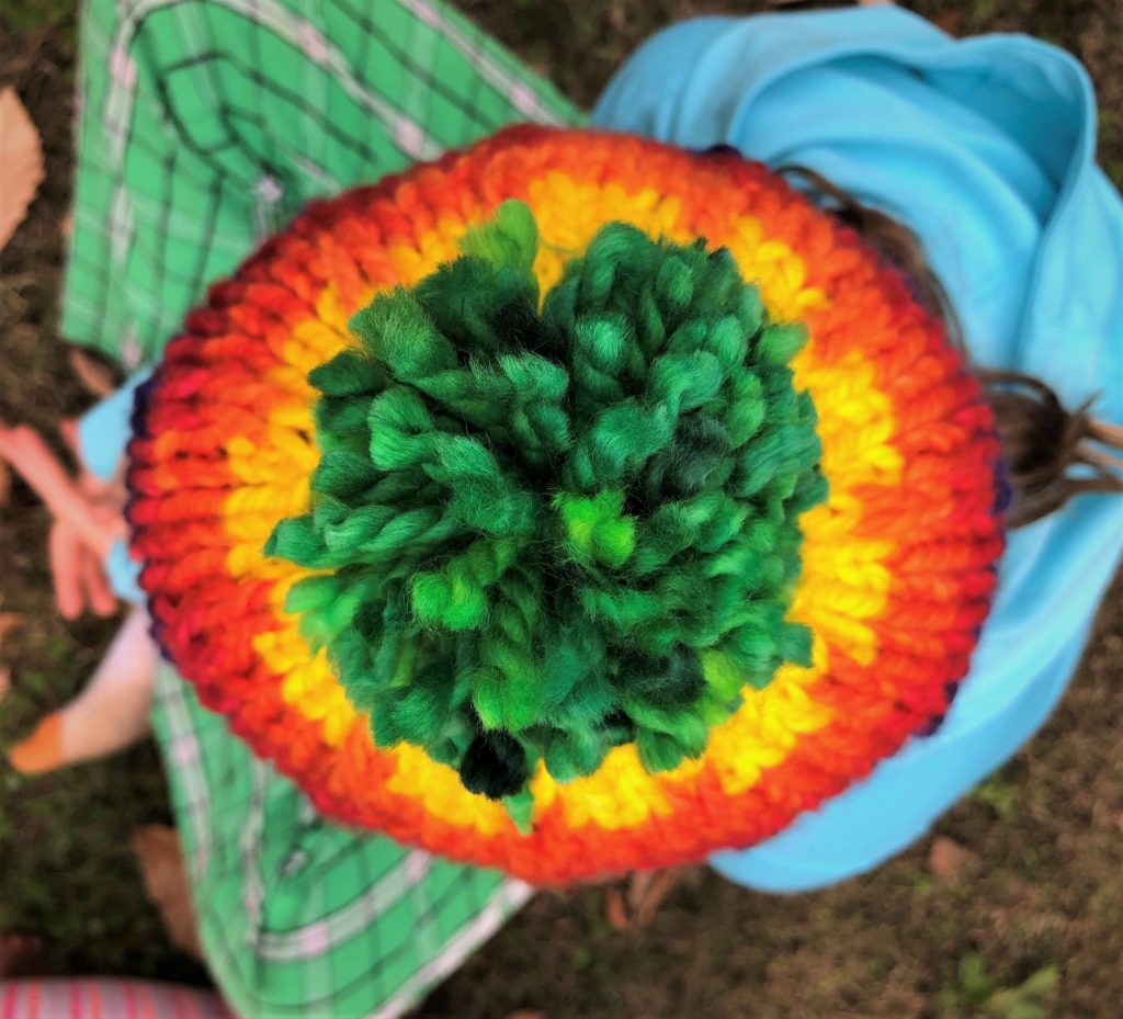 an aerial view of a rainbow knitted hat with a green pompom 