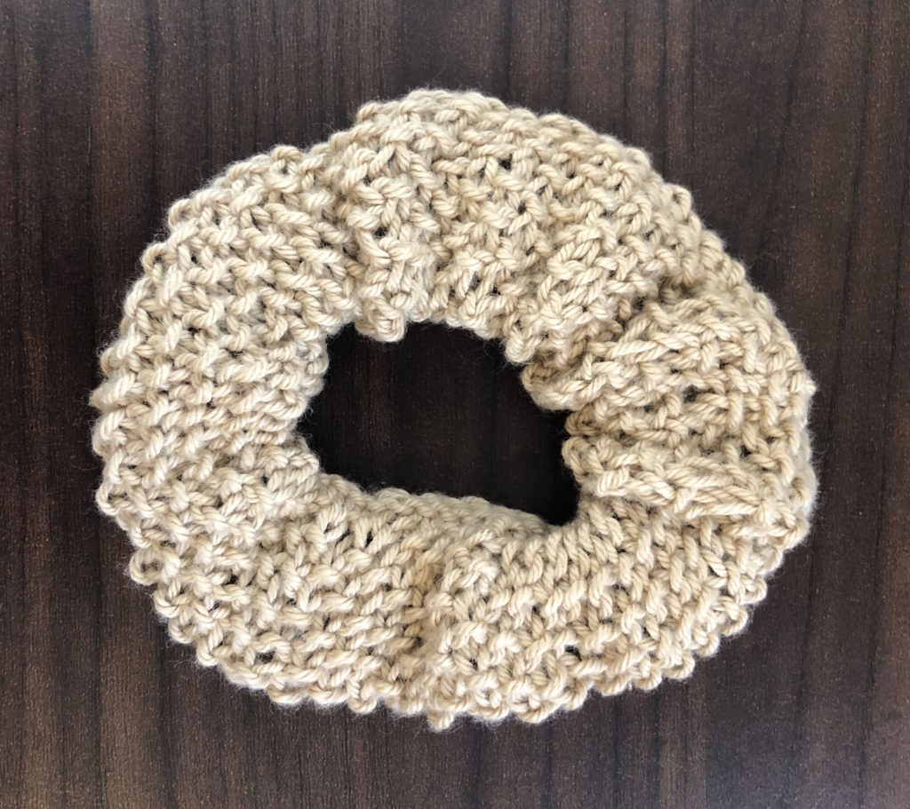 a textured knitted scrunchie on a wood panel background