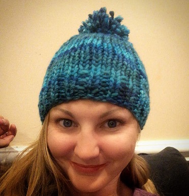 a vibrant multi-color blue knitted hat with pompom on an adult's head