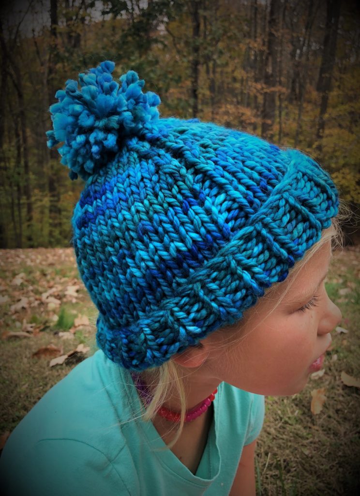 a vibrant multi-color blue knitted hat with pompom on a young girl's head