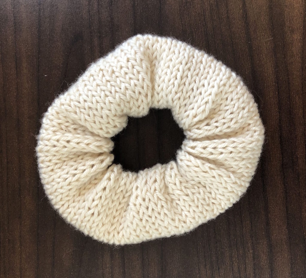 a smooth knitted scrunchie on a wood panel background