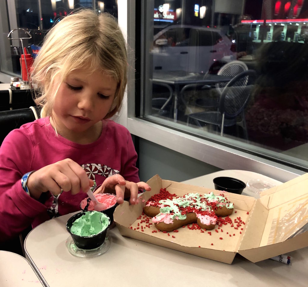 a girl decorates a gingerbread man with frosting and sprinkles