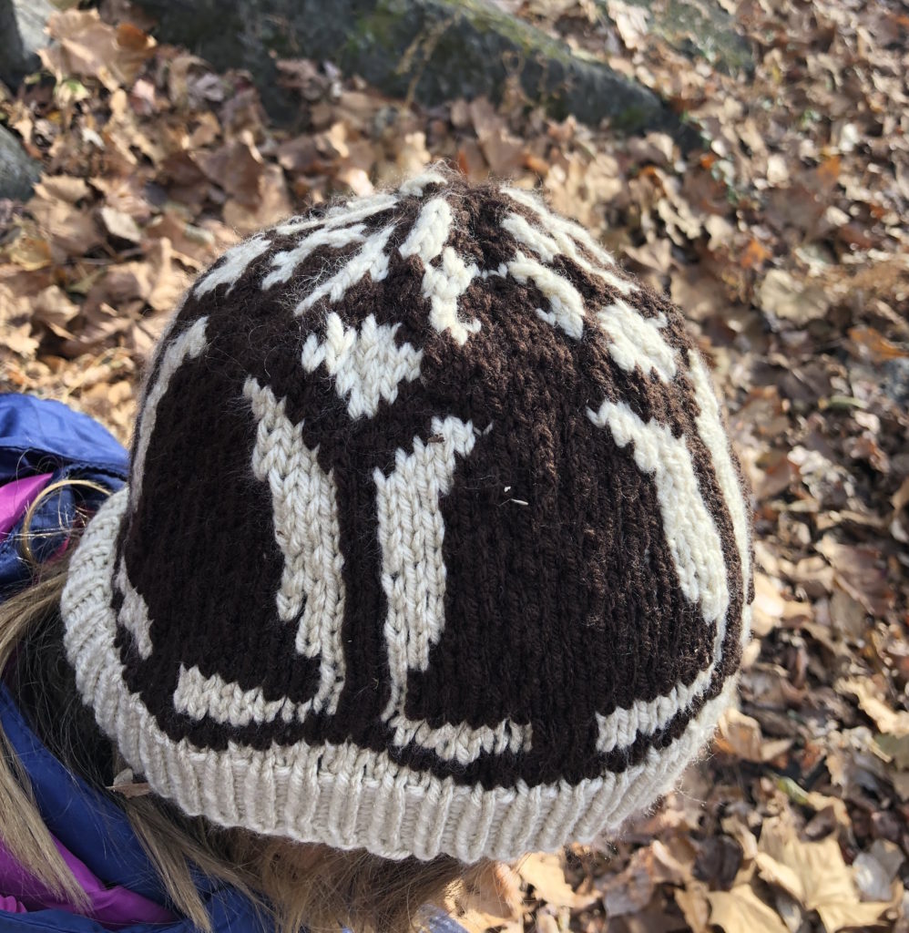 a Dahlia knitted cap features multiple paper dolls holding hands