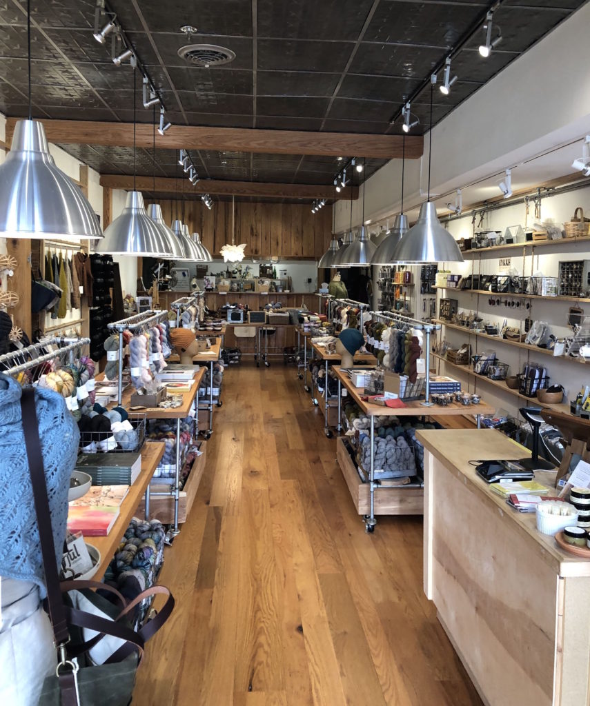 the interior of EWE Fine Fiber Goods: minimalist wooden and metal tables and shelves are lined with yarn under hanging lights