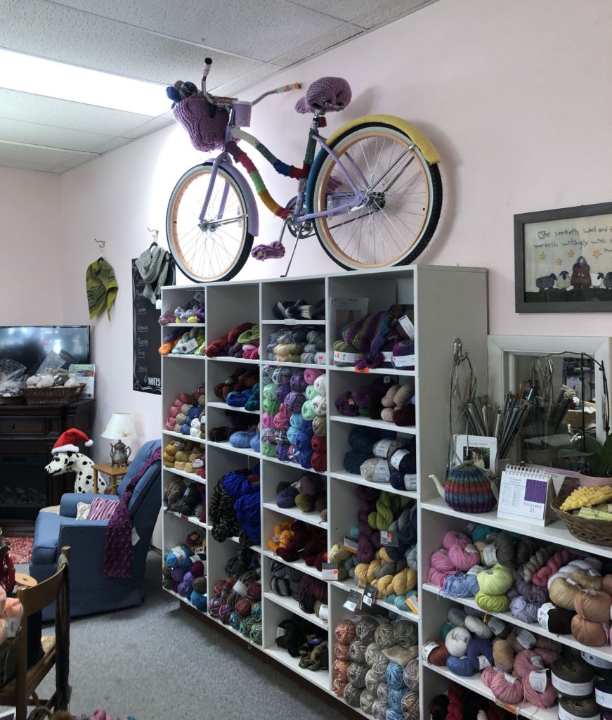 the interior of Laughing Sheep Yarns: shelves of skeins of yarn and a yarn-bombed bicycle