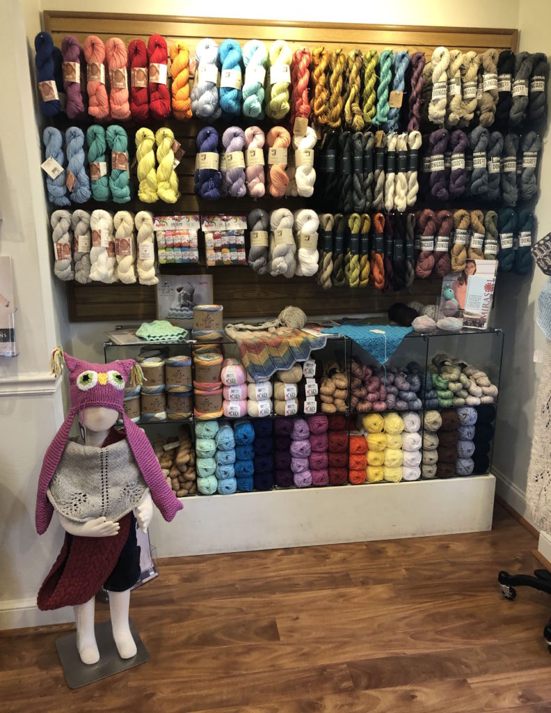 skeins of yarn hang behind a child-sized mannequin dressed head-to-toe in handknits