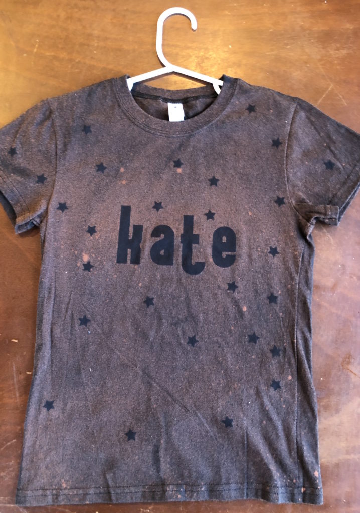 the same shirt with stickers removed after bleach has been applied reveals dark letters and stars