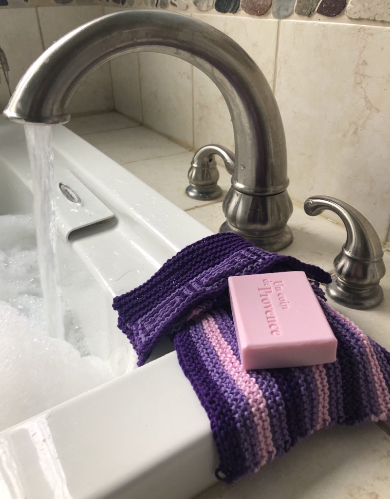 a bathtub fills while two washcloths and a bar of soap wait to be used