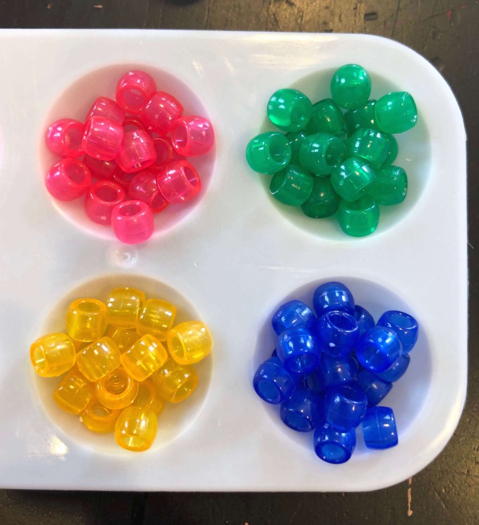 translucent pony beads arranged by color in the wells of a paint palette