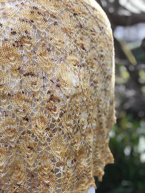a close-up of a knitted leaf-shaped shawl on a woman's back