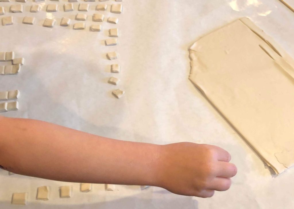 a child places clay squares on a sheet of wax paper