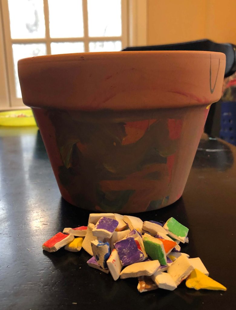 a pile of multicolored air-dry clay tiles rests, ready to use, in front of a painted terracotta flowerpot