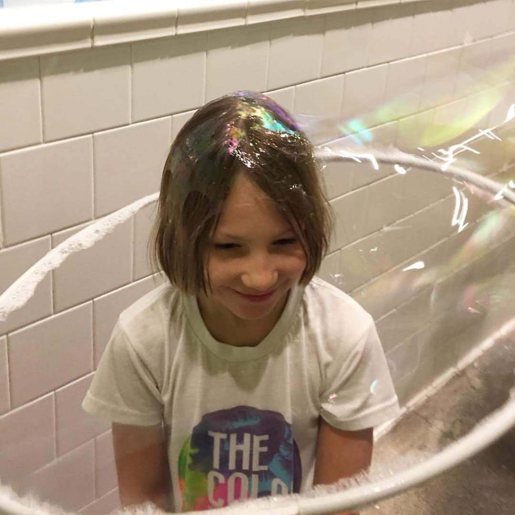 a girl smiles as a giant bubble is formed around her