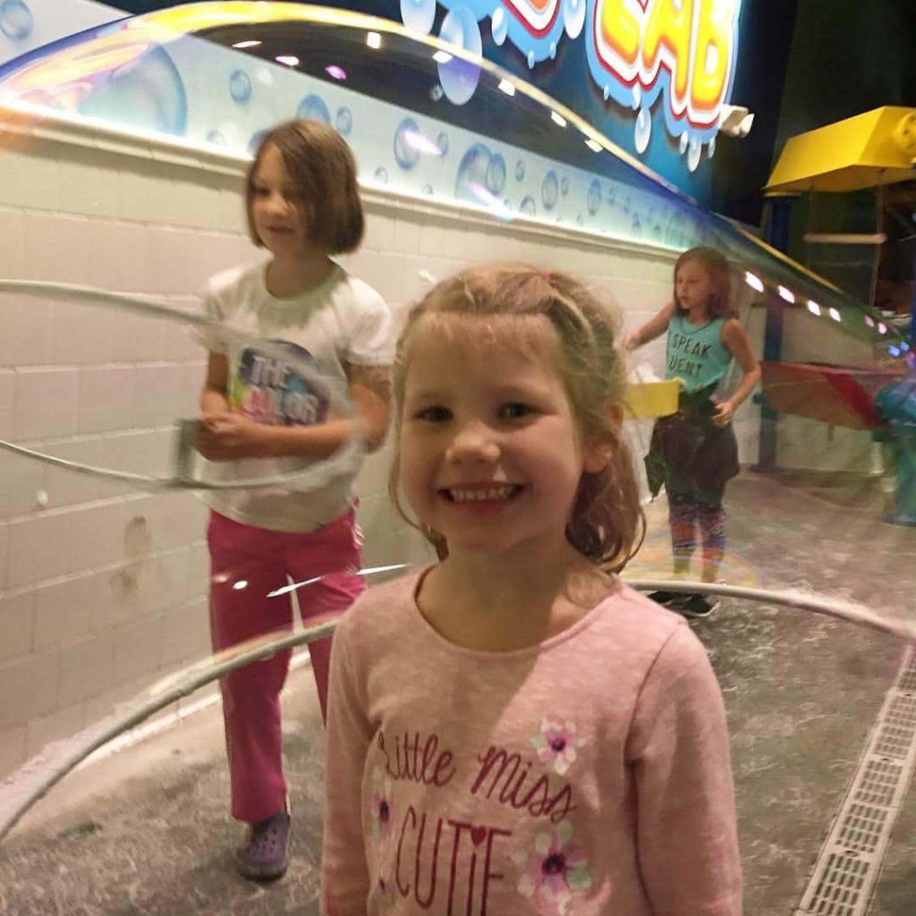 a girl smiles as a giant bubble is formed around her