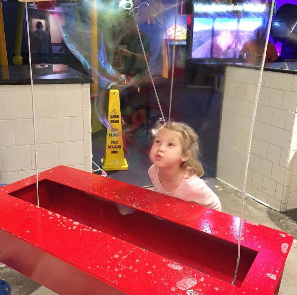 a girl blows on a giant bubble wall and bubbles form