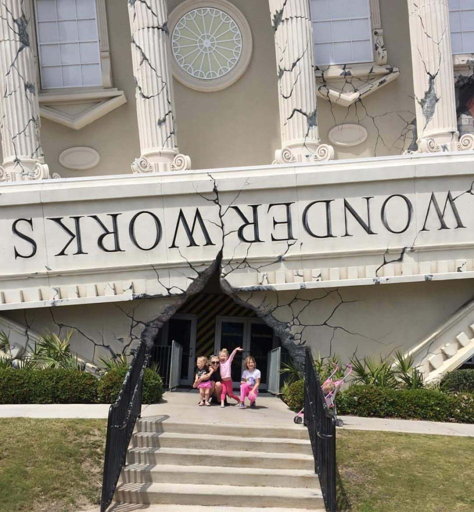 children wait outside of an upside-down building with ornate columns that appears to have cracked open