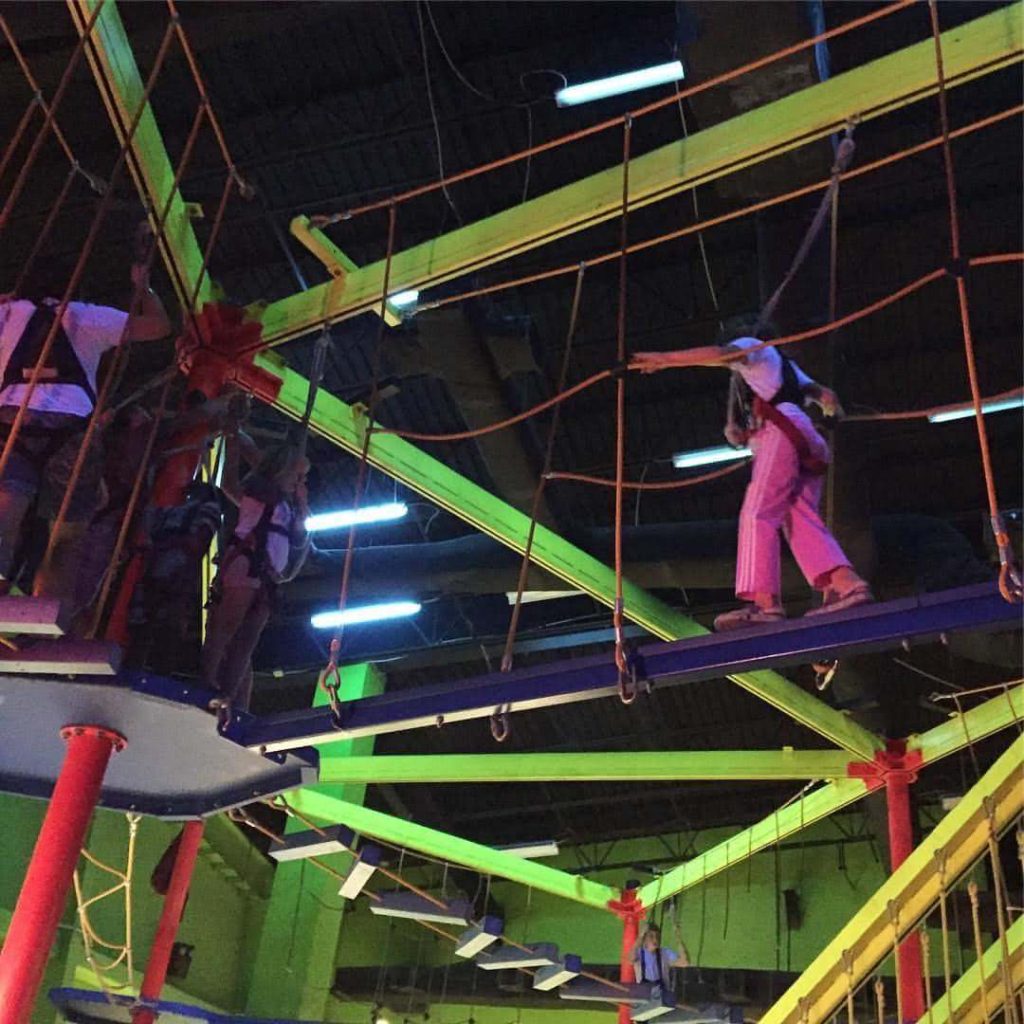 a young girl climbs across a high-ropes course while strapped into a harness