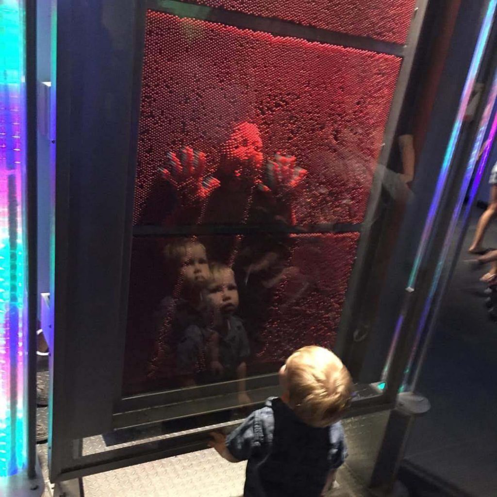 a young boy reacts to the impression of his sister on a pin board