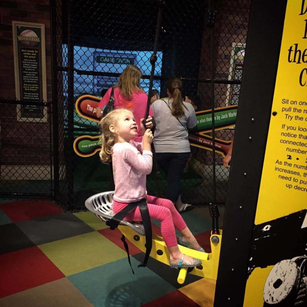 a young girl sits in a chair attached to a pulley and uses a rope to lift herself up