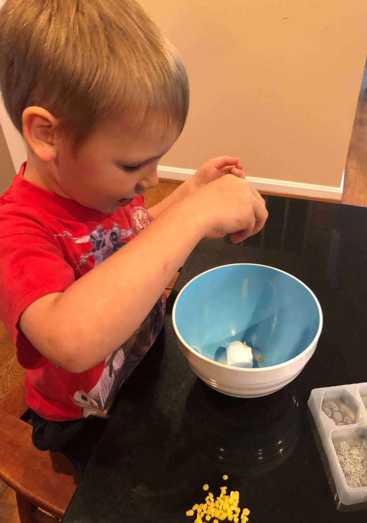 a young boy drops oil into a plastic bowl filled with soap base