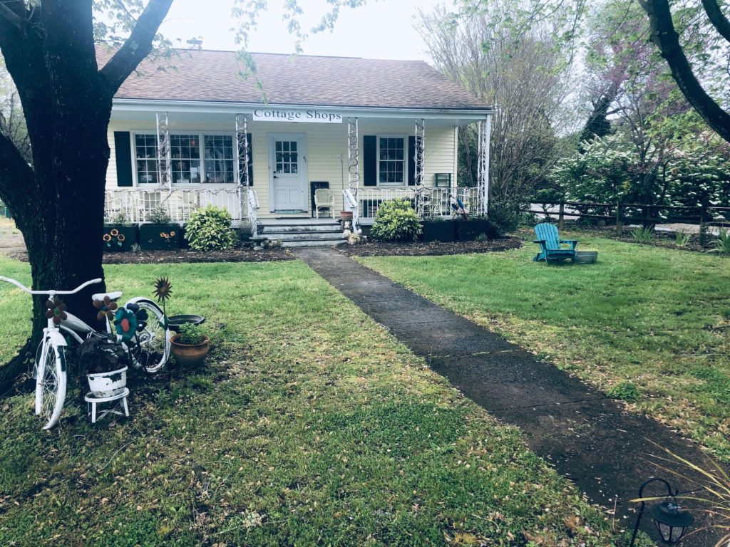 exterior of a bright cottage with a bicycle and Adirondack outside Knit Wit Yarn Shop